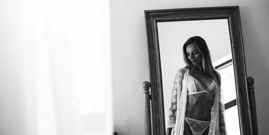 Confident woman in lace lingerie looking at herself in a mirror.